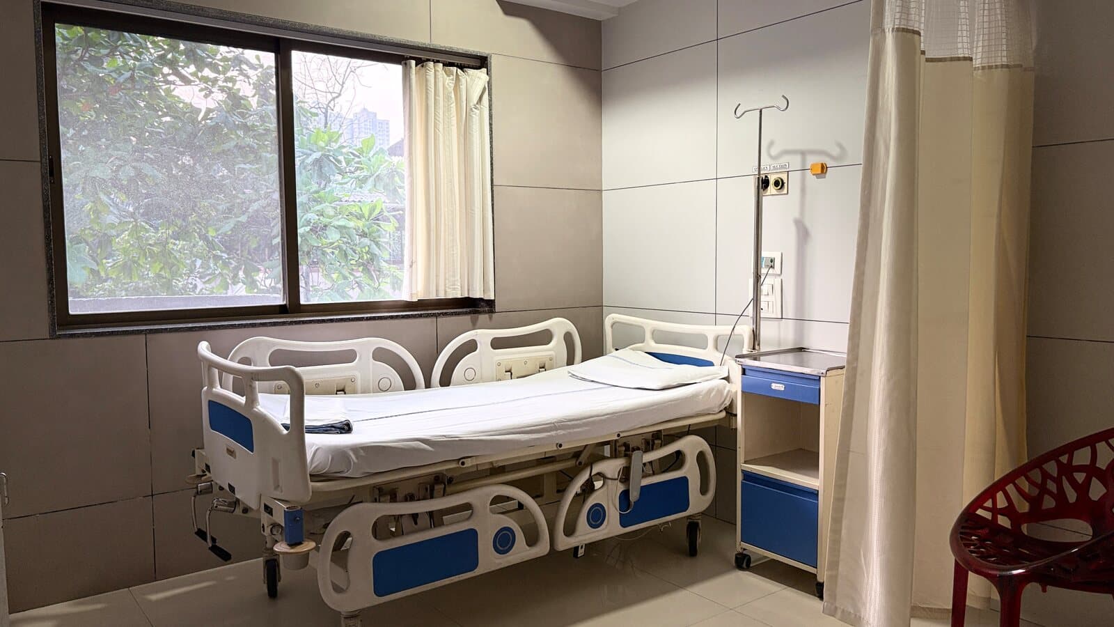 A patient room at THC Hospital, the bed beside a window looking out onto trees