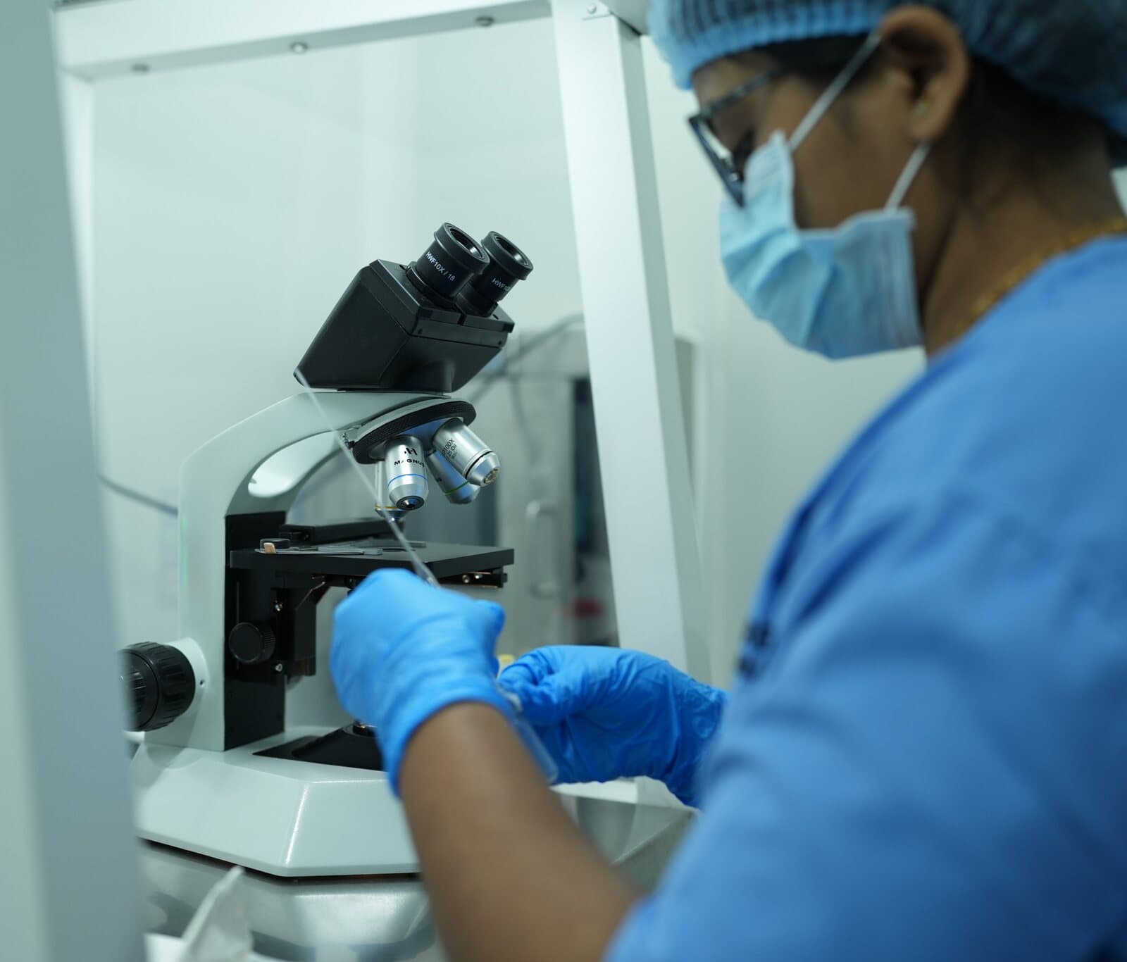 A laboratory technician in gloves looking at a sample under a microscope